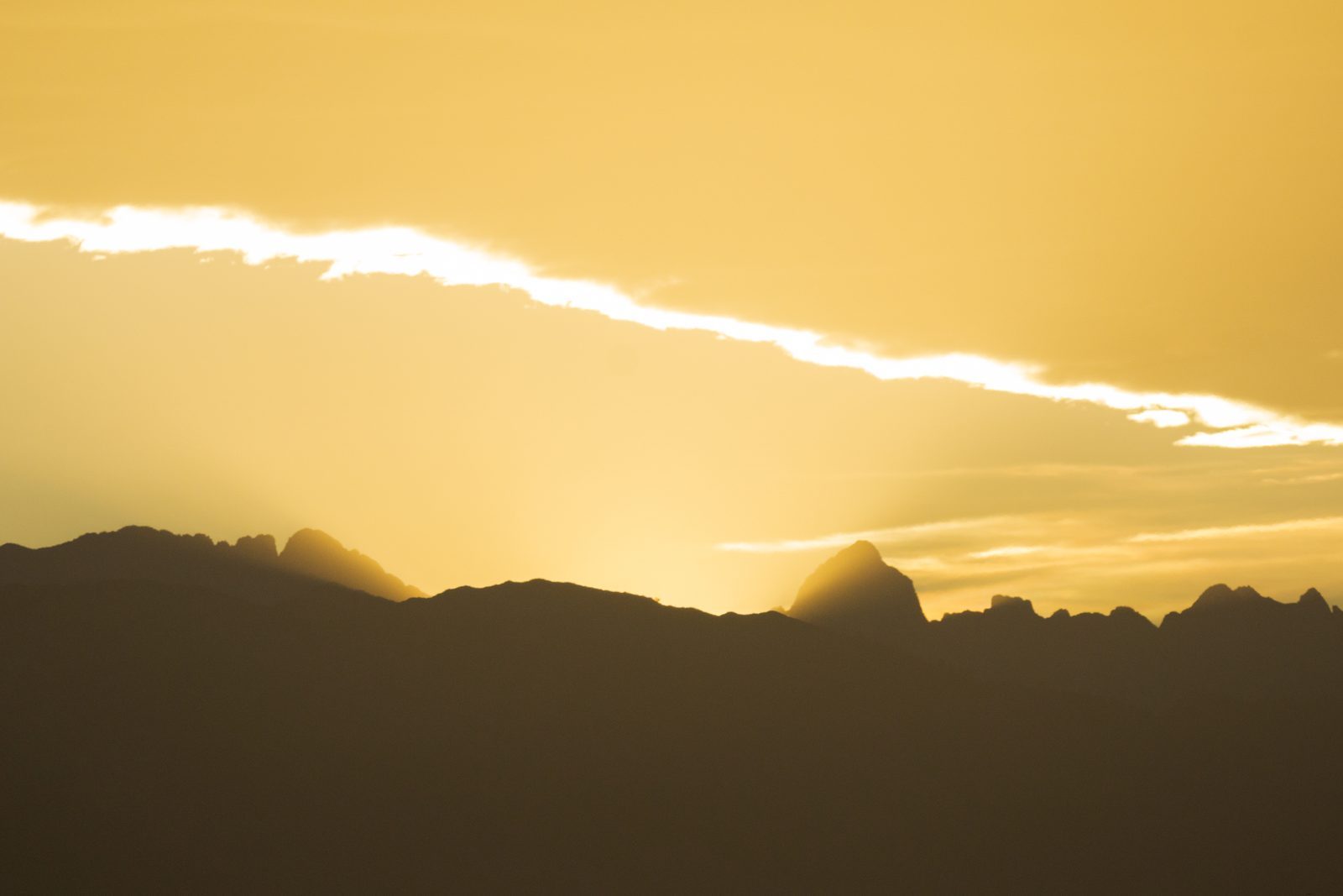 As the sun slips behind jagged peaks, golden light lingers like a quiet promise—reminding us that even in parting, warmth remains.