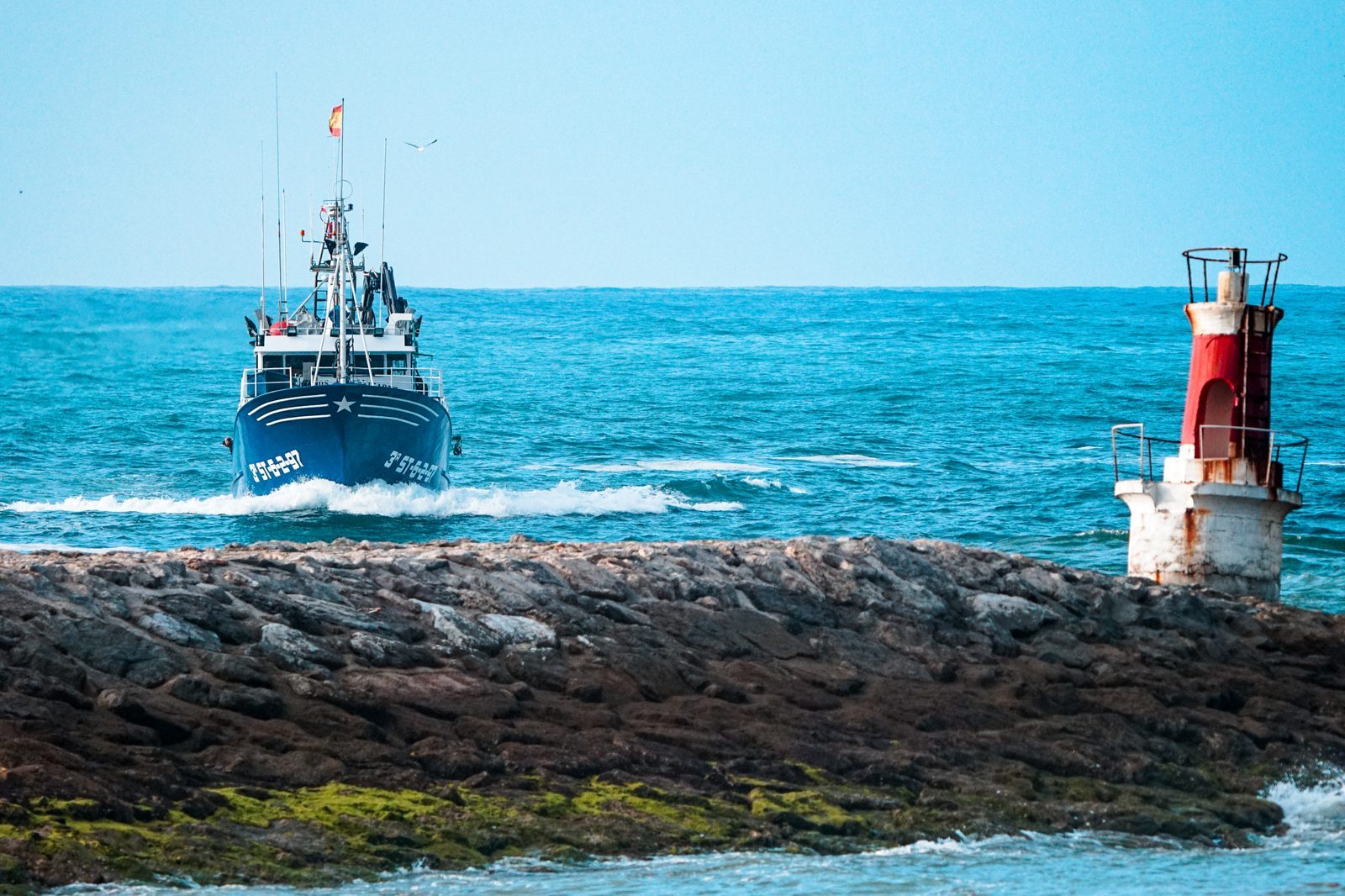 Guided home by a weathered lighthouse, the fishing boat cuts through the waves, carrying the quiet promise of return to those waiting on shore.