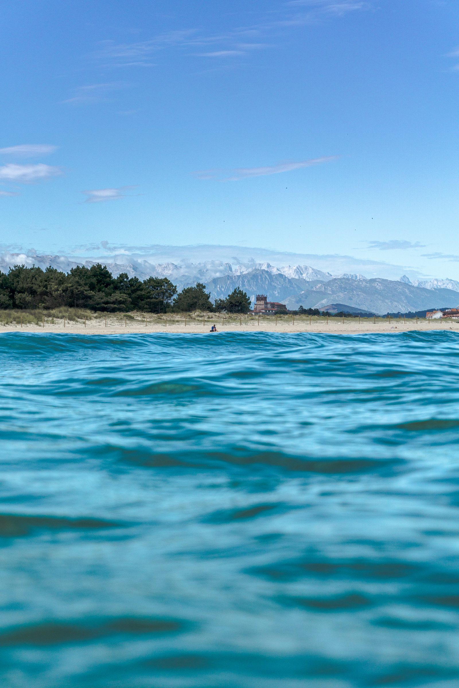 Where the turquoise sea meets snow-capped peaks, one quiet figure on the shore reminds us that love, too, finds beauty in stillness.