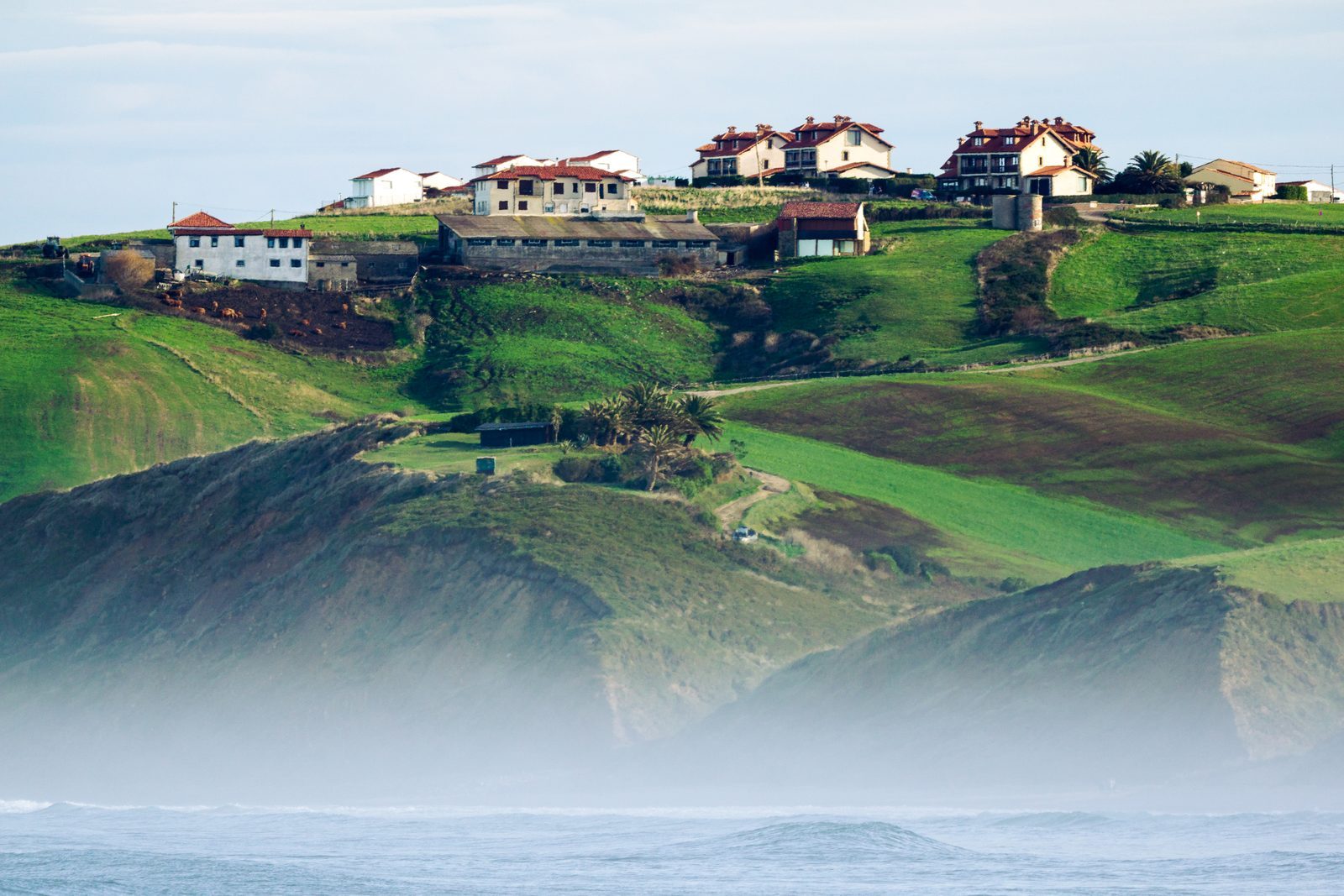 Where green hills meet the misty sea, a quiet village rests—reminding us that home is simply love, gathered gently on the horizon.