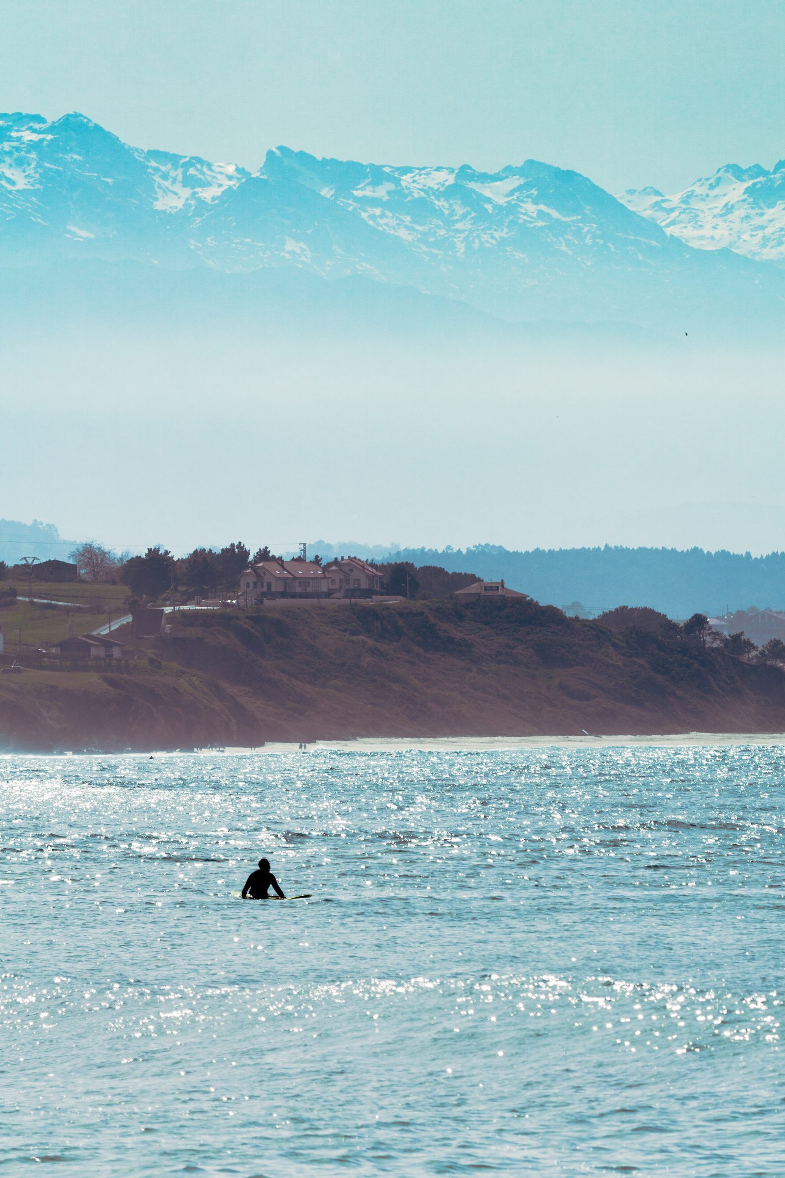 Alone on the vast, glittering sea, the surfer waits patiently—a quiet reminder that even solitude can feel like being held by something greater.