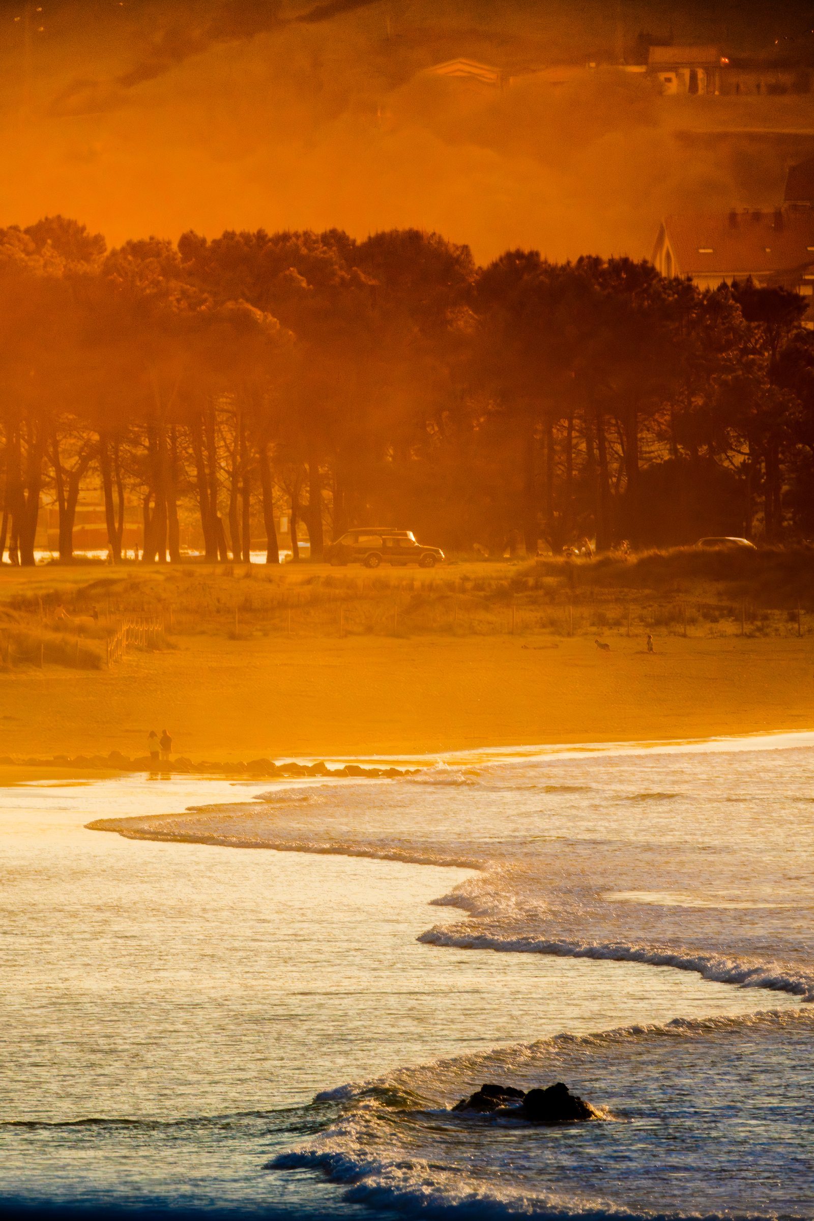 Two silhouettes walk hand in hand along the shore, wrapped in golden light, as the world fades softly into warmth around them.