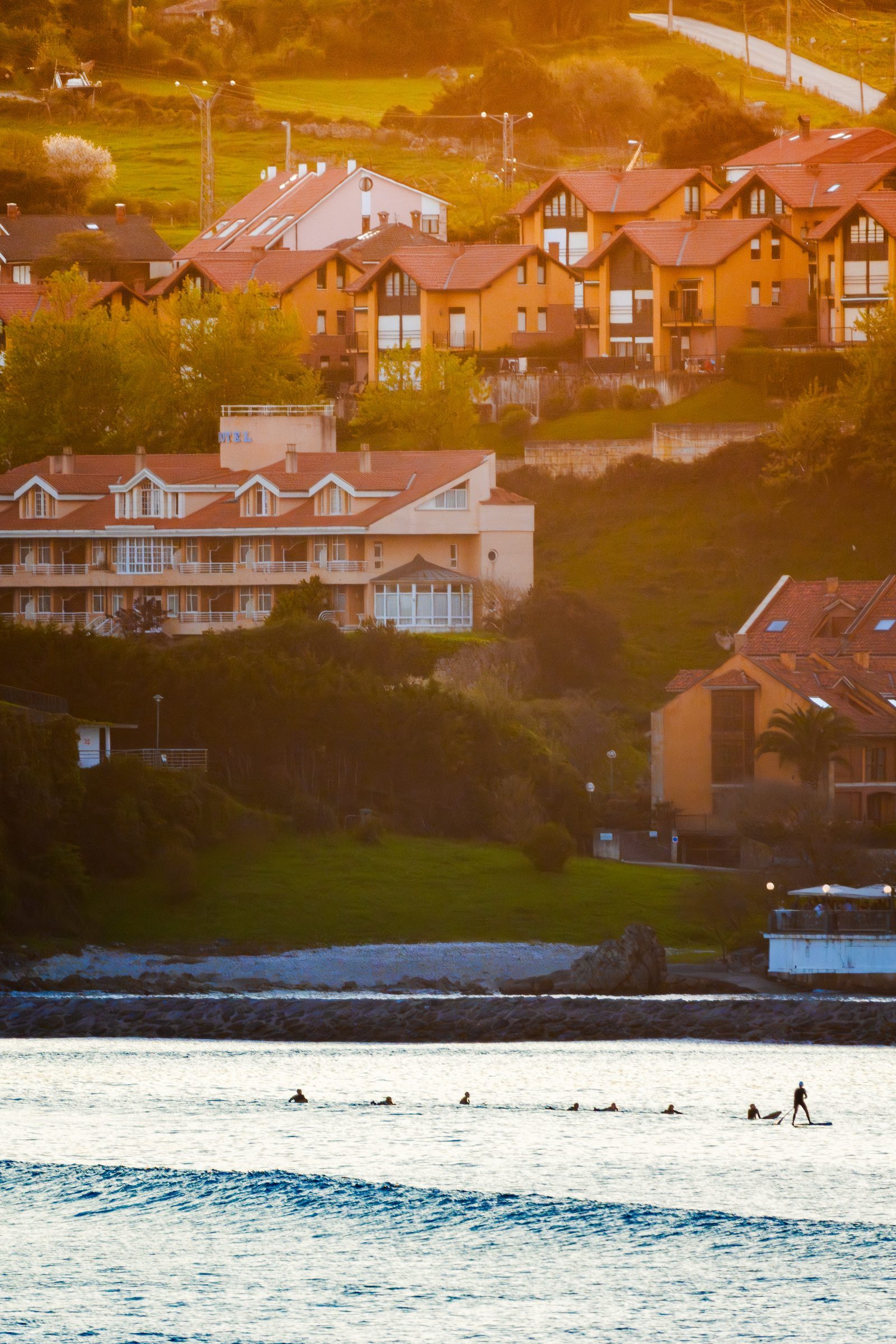 Golden light spills over the hillside town as surfers wait together in the water, a quiet reminder that connection often happens in stillness.